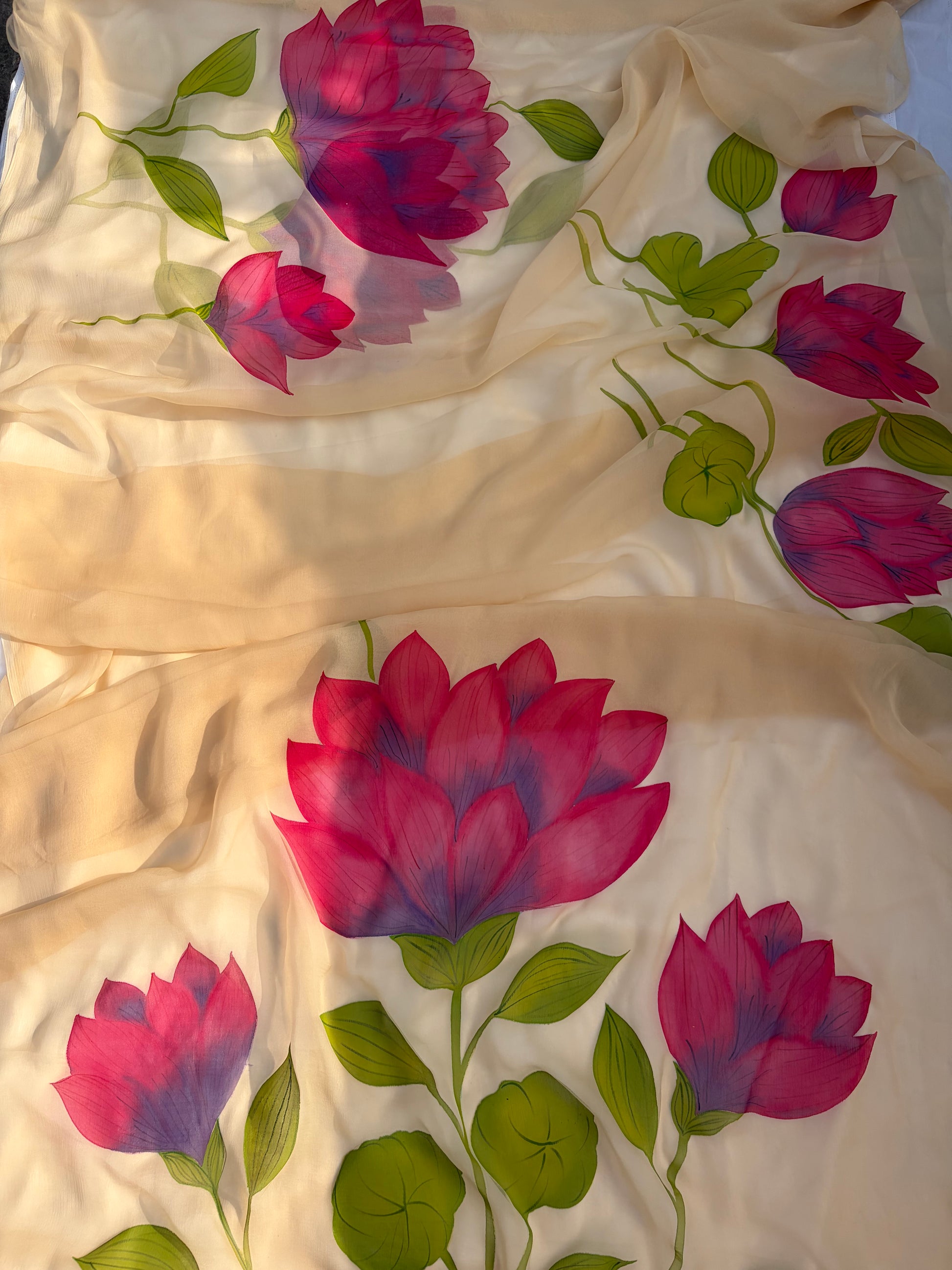 Close-up of a cream-colored chiffon saree featuring large, vibrant pink and purple hand-painted lotus flowers with green leaves.